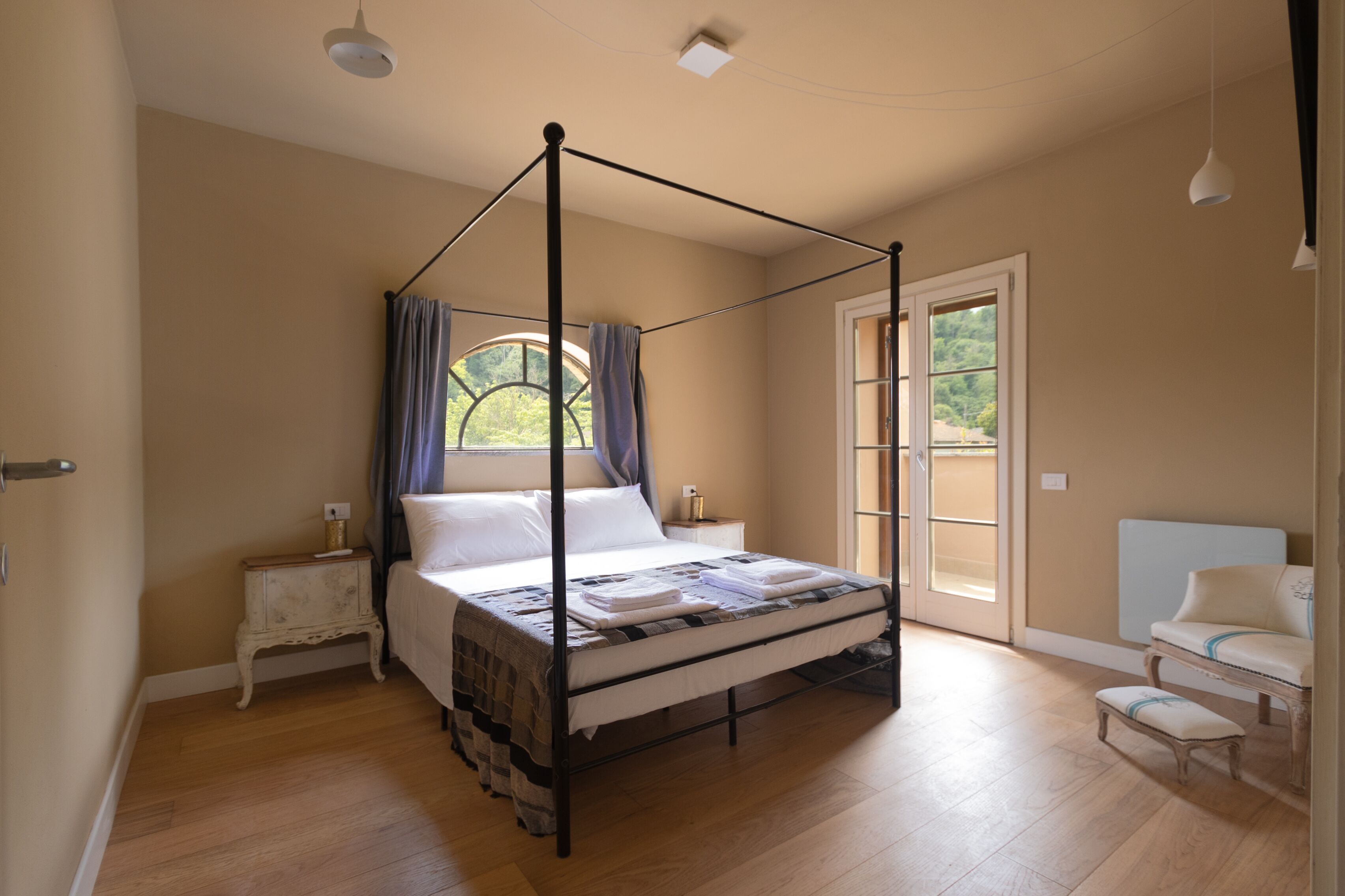 Un dormitorio con cama con dosel, una mesita de noche, una silla y vistas al exterior a través de una ventana.