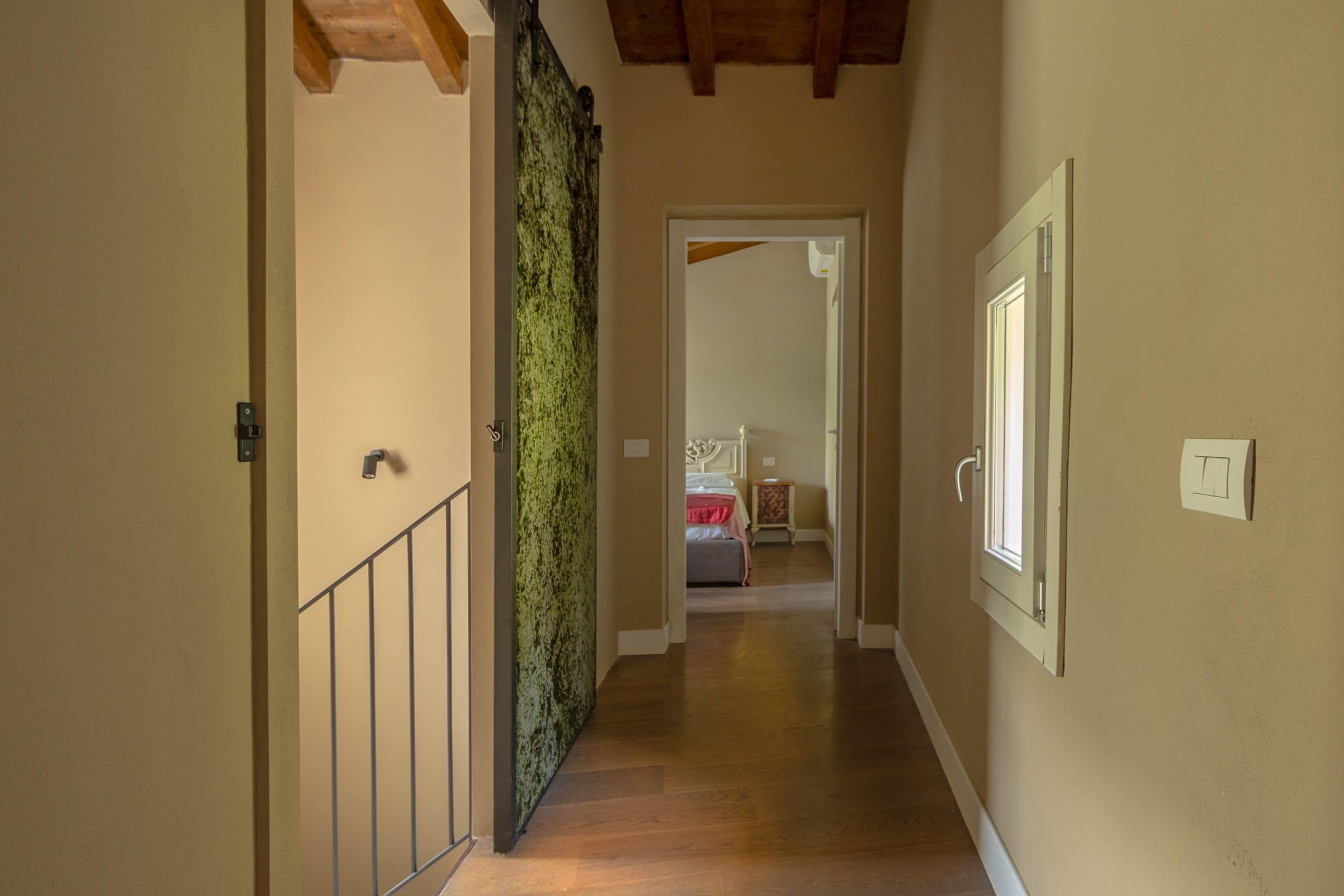 A hallway with wooden flooring, a metal railing on one side, and a door with a green textured wall.