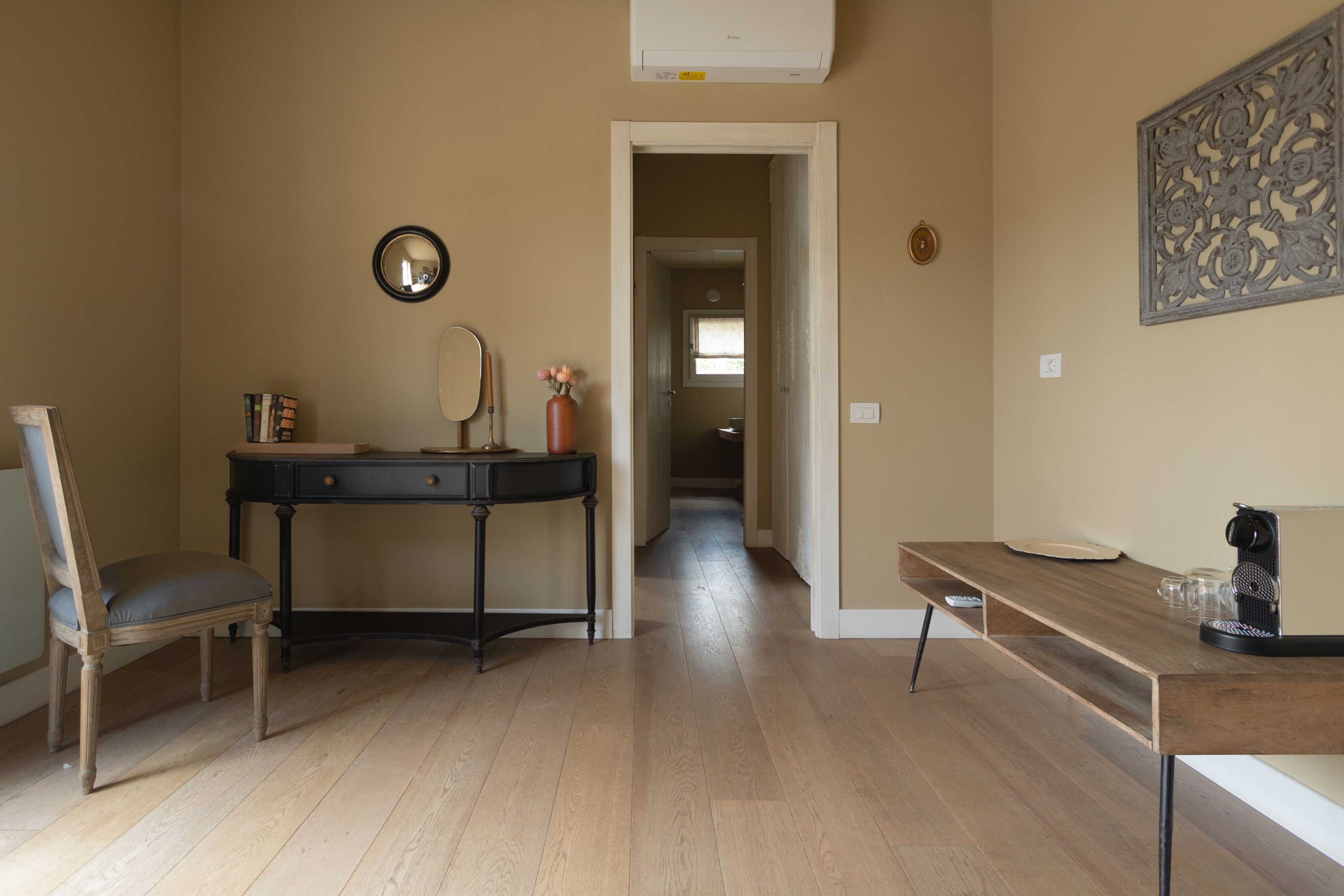 Una habitación con escritorio de madera, una silla, un espejo y un adorno en la pared.