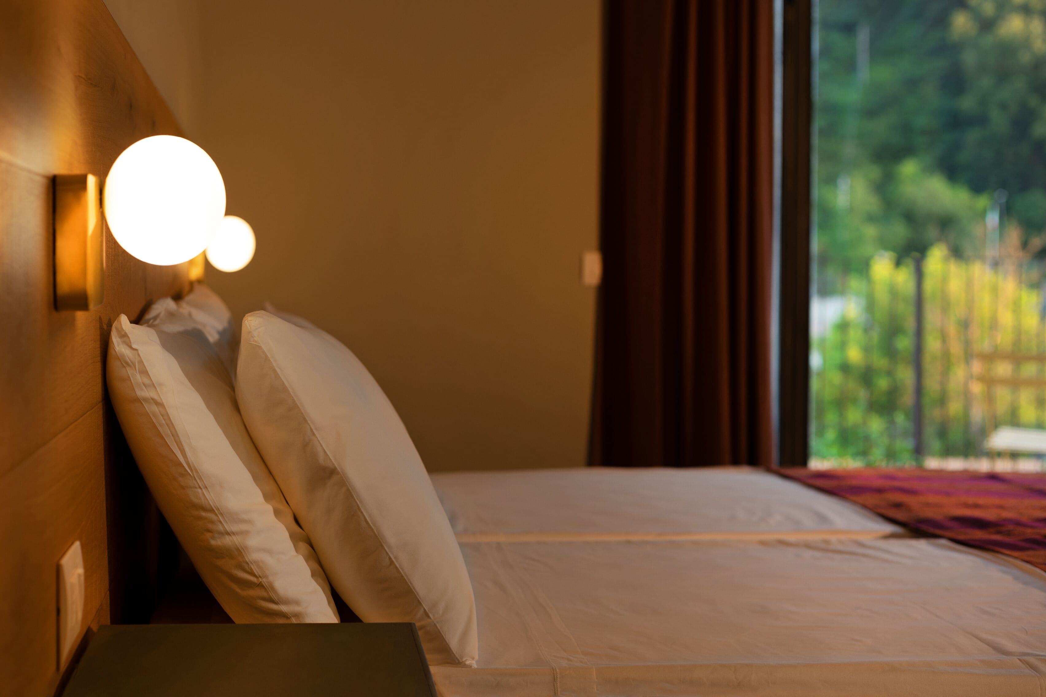 A hotel room with a bed, pillows, a nightstand, and a wall-mounted light fixture.