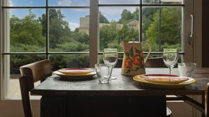 A dining table with plates, glasses, and a pitcher, set against a window with a view of greenery and buildings. - Luce Boutique Hotel (Fortunago)