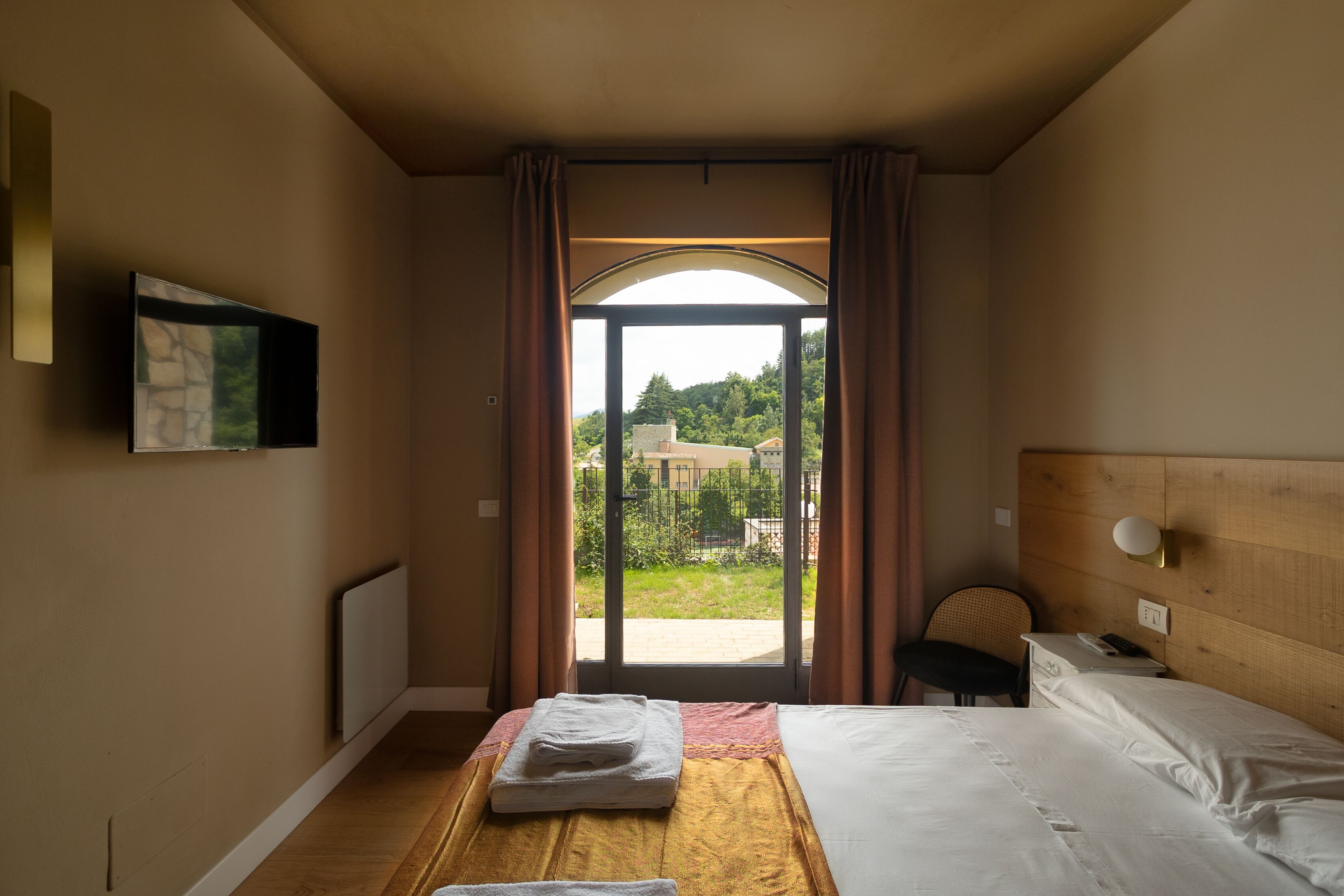 A hotel room with a bed, a desk, a chair, a TV, and a view of the outdoors.