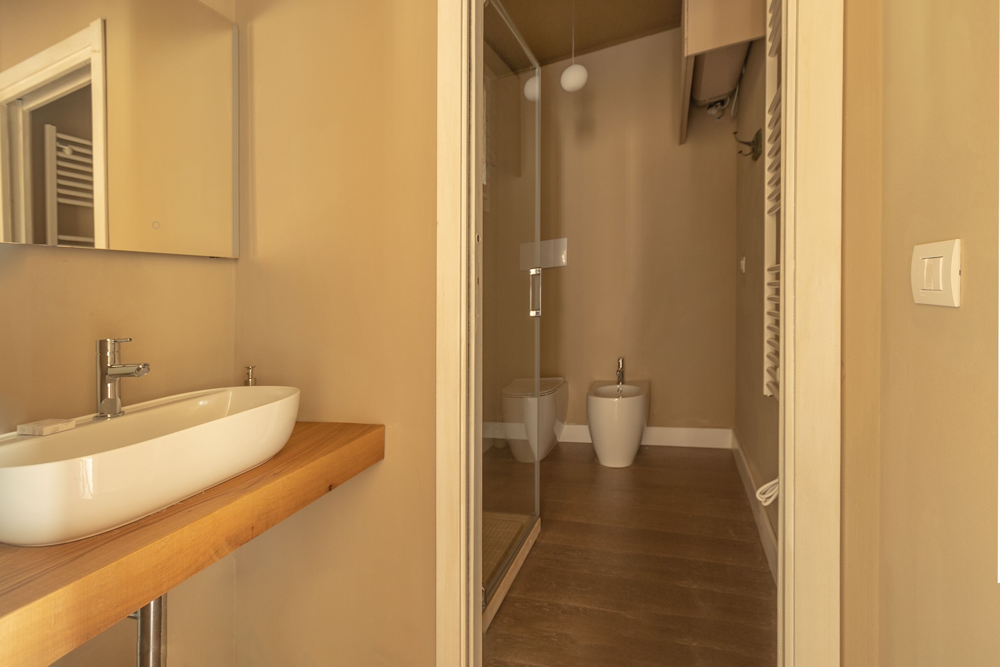 Un bagno moderno con un ampio lavandino bianco, uno specchio e una cabina doccia.