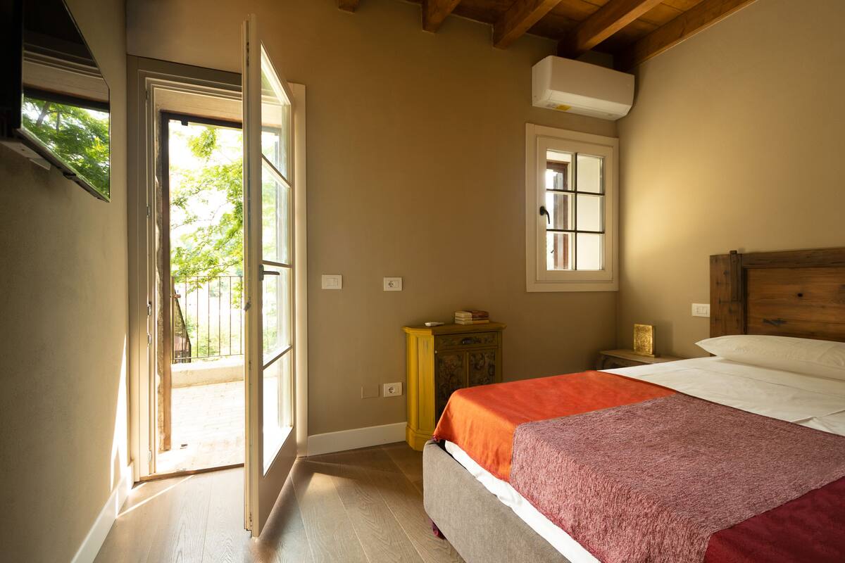 A bedroom with a bed, a wooden headboard, a window, and a door leading to an outdoor area.