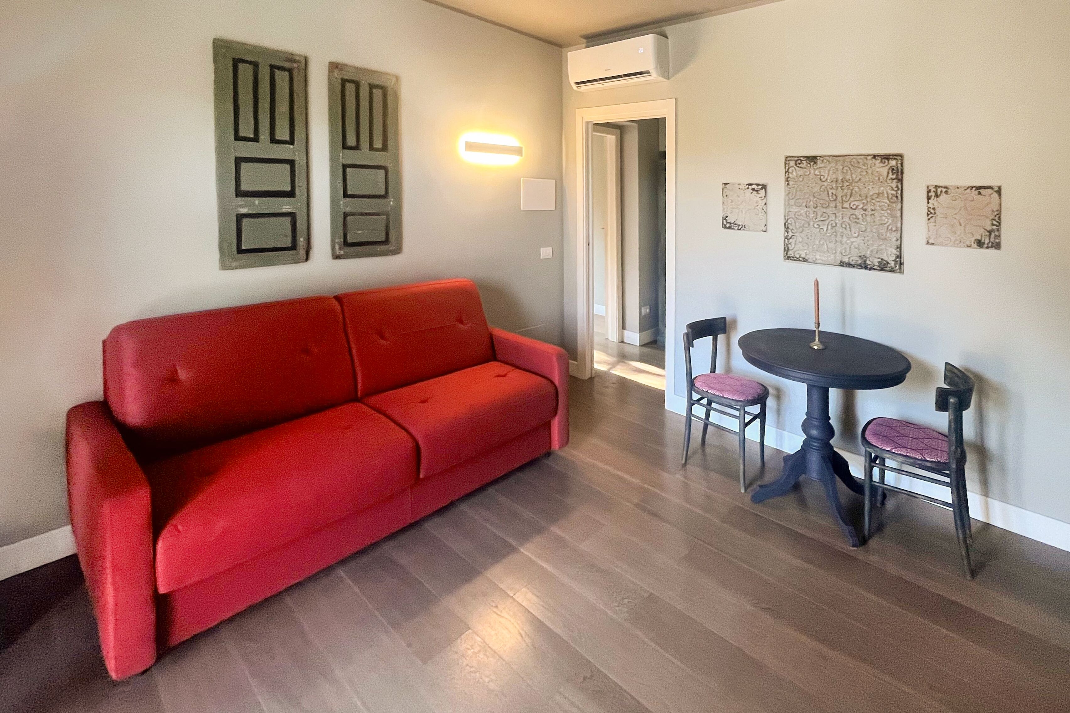 Un soggiorno con un divano rosso, un tavolino rotondo con due sedie e decorazioni murali.