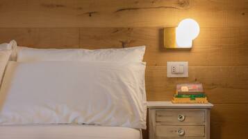 A neatly made bed with white linens, a bedside table with a stack of books, and a wall-mounted light fixture.