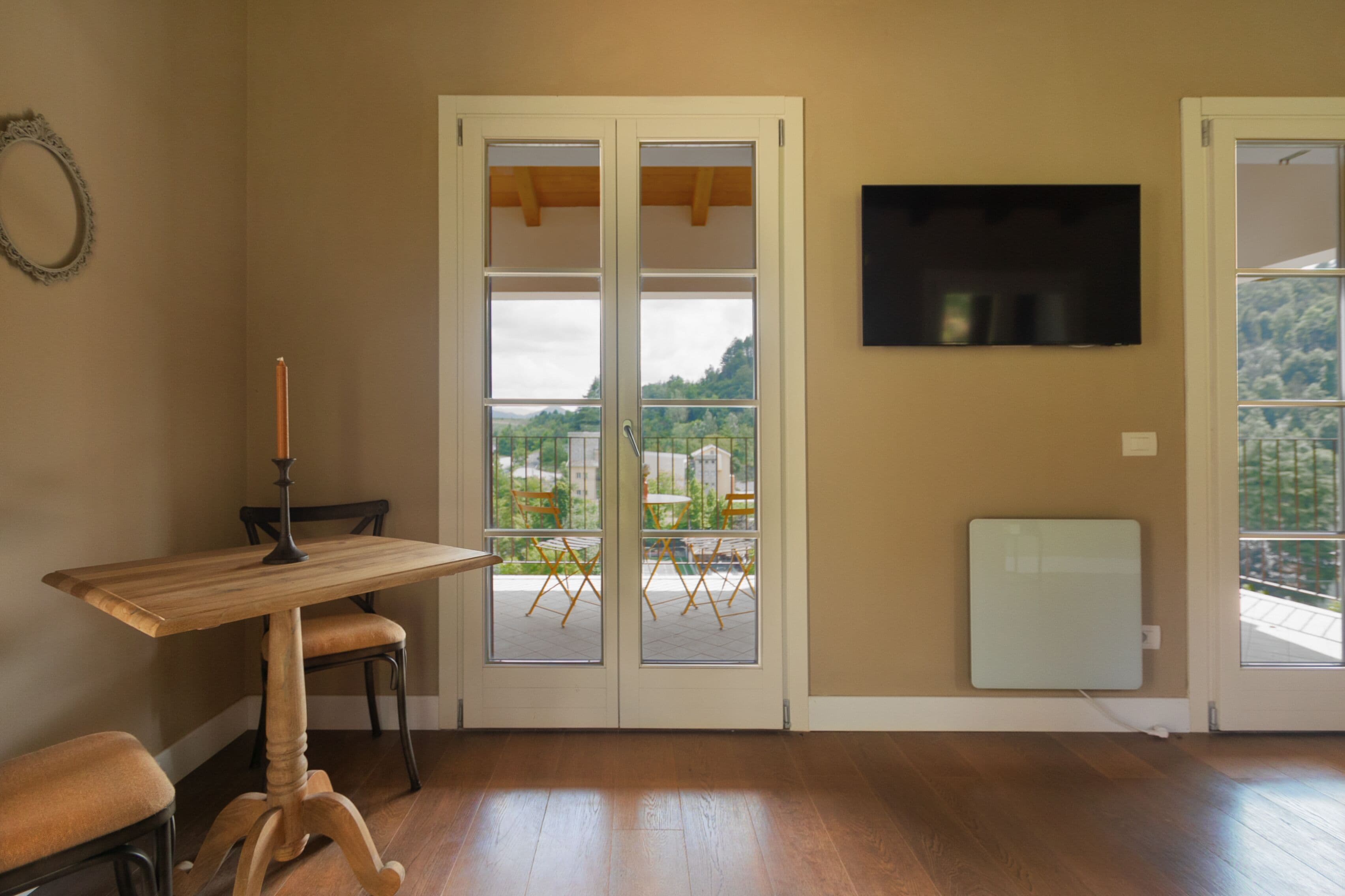A room with a wooden table and chairs, a large window with a view of greenery, and a mounted television.