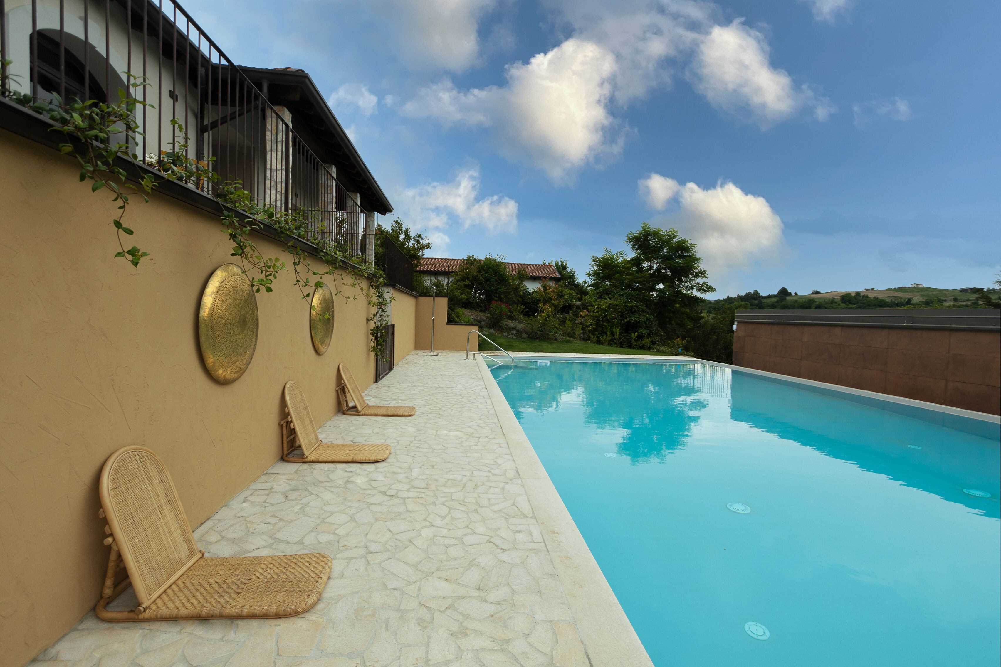 Una piscina con sillas de descanso, un patio con baldosas de piedra y un edificio con balcón.