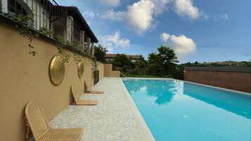 Una piscina con sillas de descanso, un patio con baldosas de piedra y un edificio con balcón.
