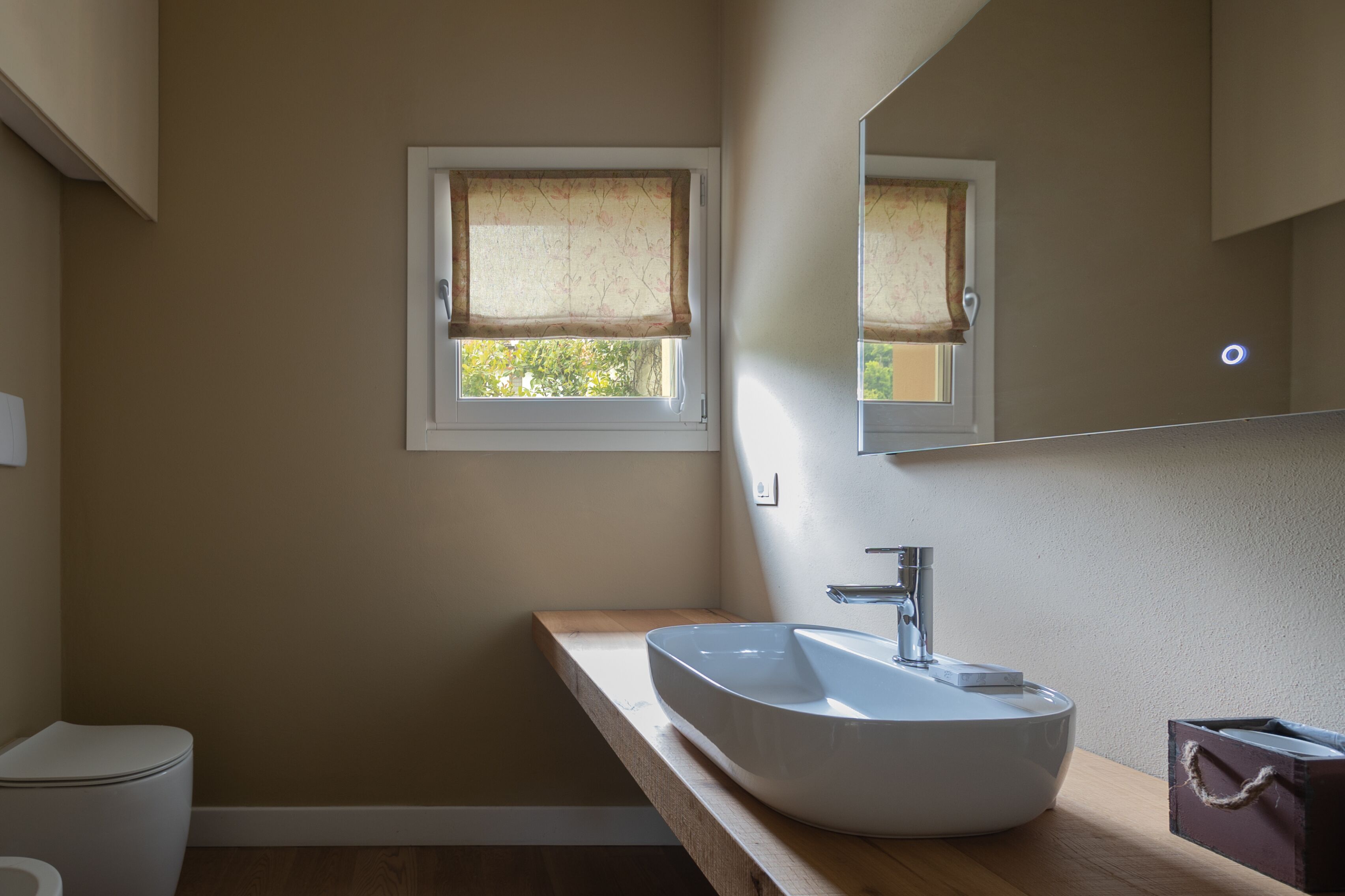 A bathroom with a white sink, a wooden countertop, a window with a curtain, and a mirror above the sink.