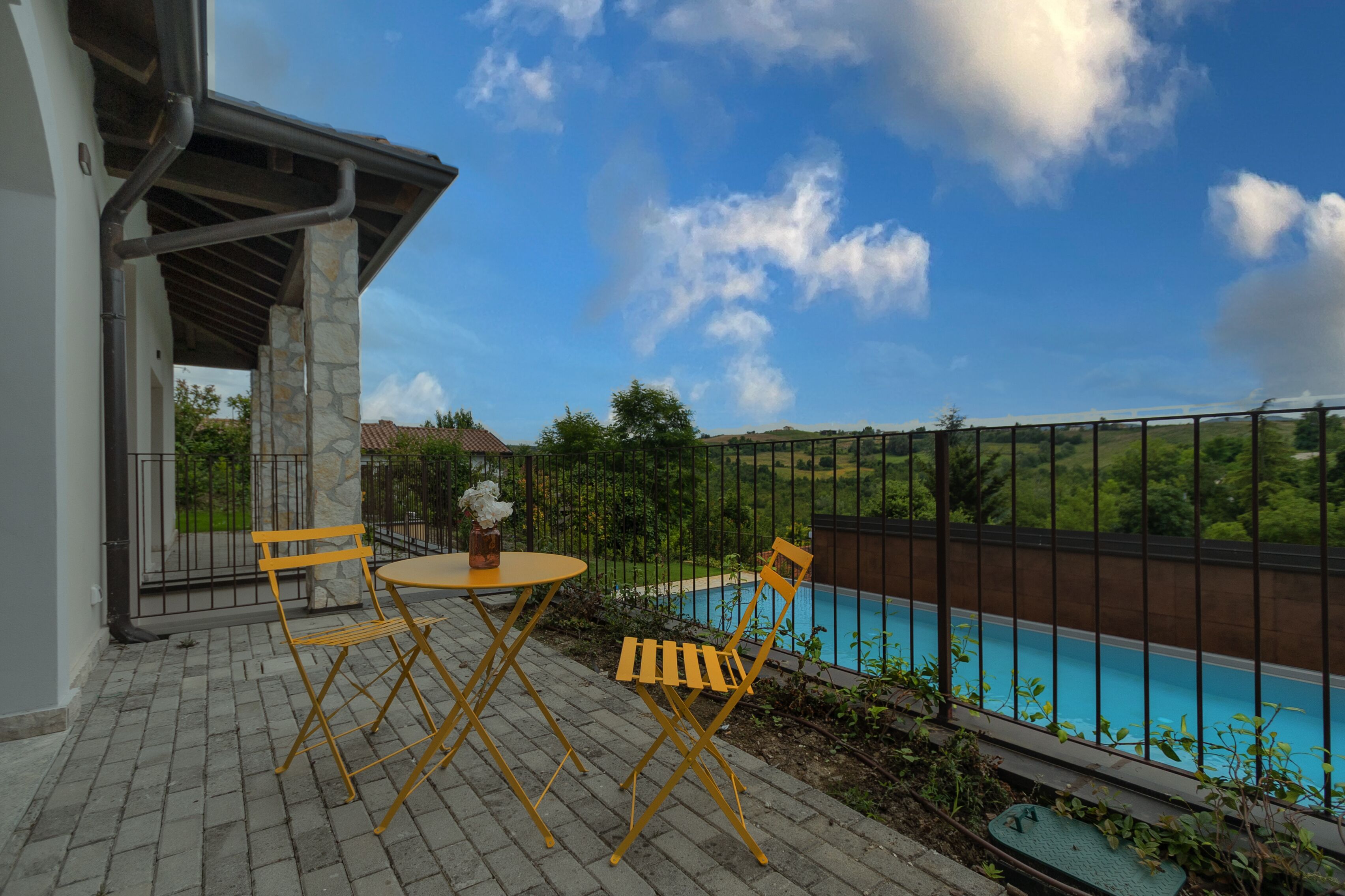 Une terrasse avec une piscine, des piliers en pierre et des chaises jaunes.