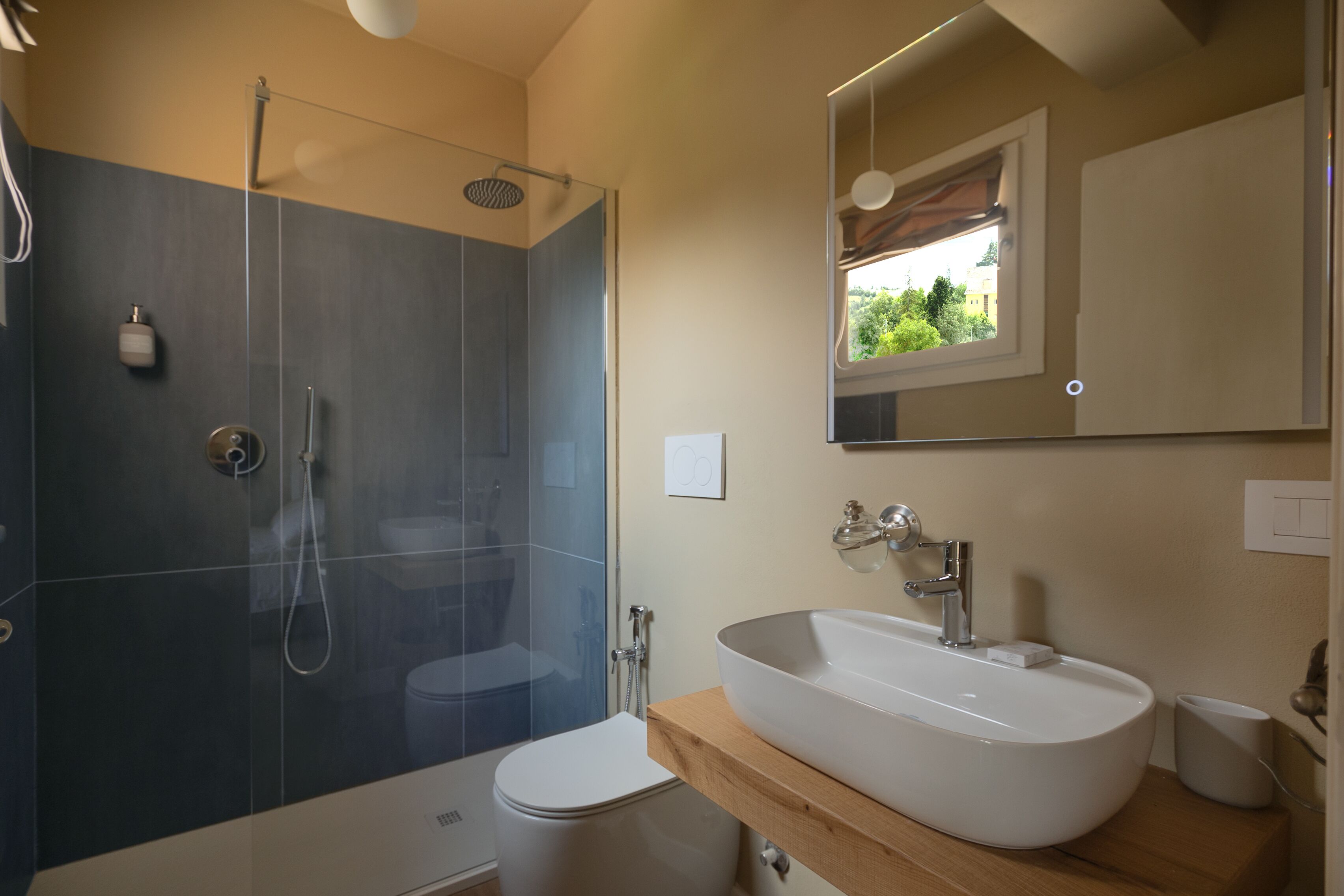 Un baño moderno con ducha envuelta en vidrio, inodoro blanco y un lavabo grande tipo cuenco.