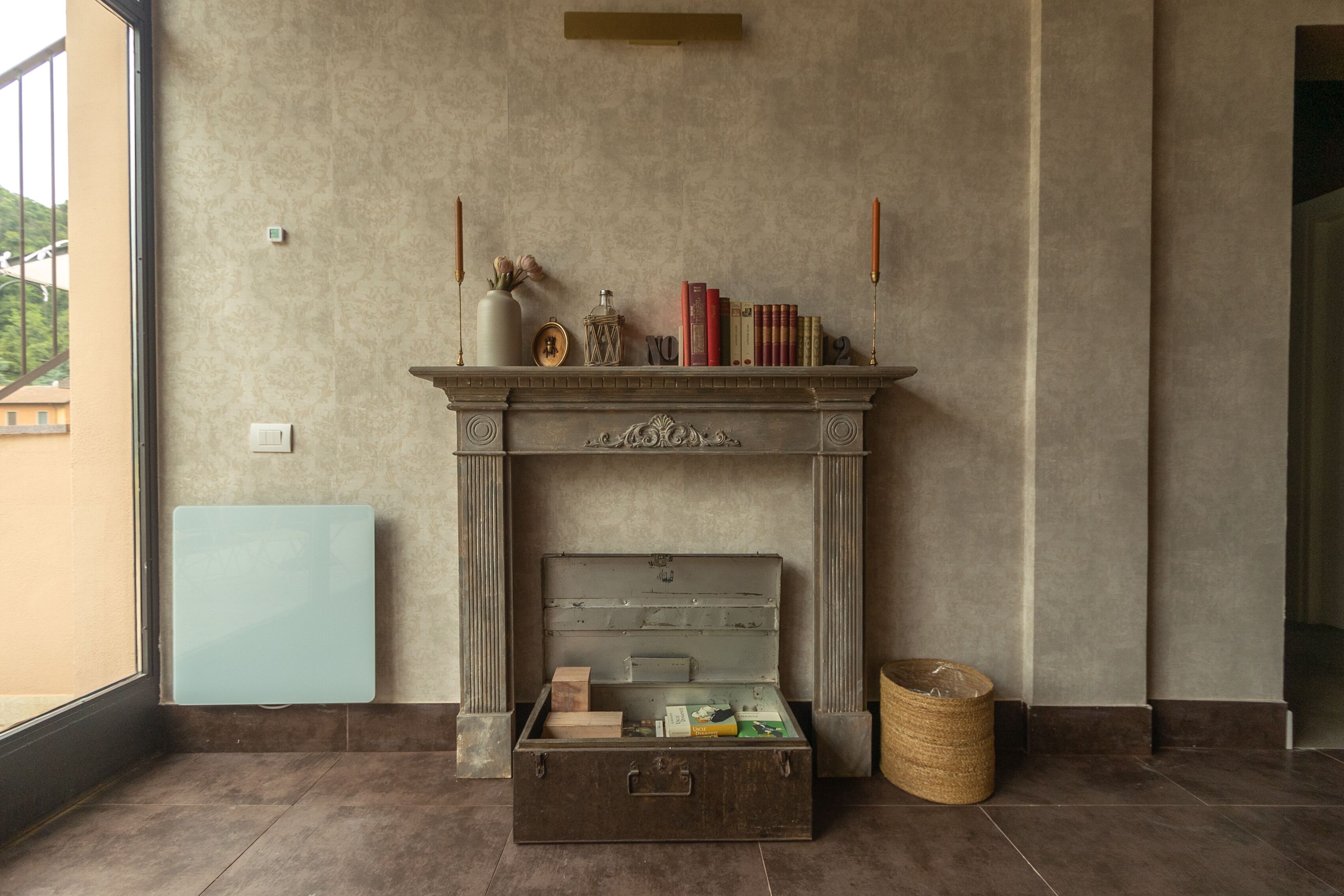 A room with a fireplace, a large window, and a storage chest.