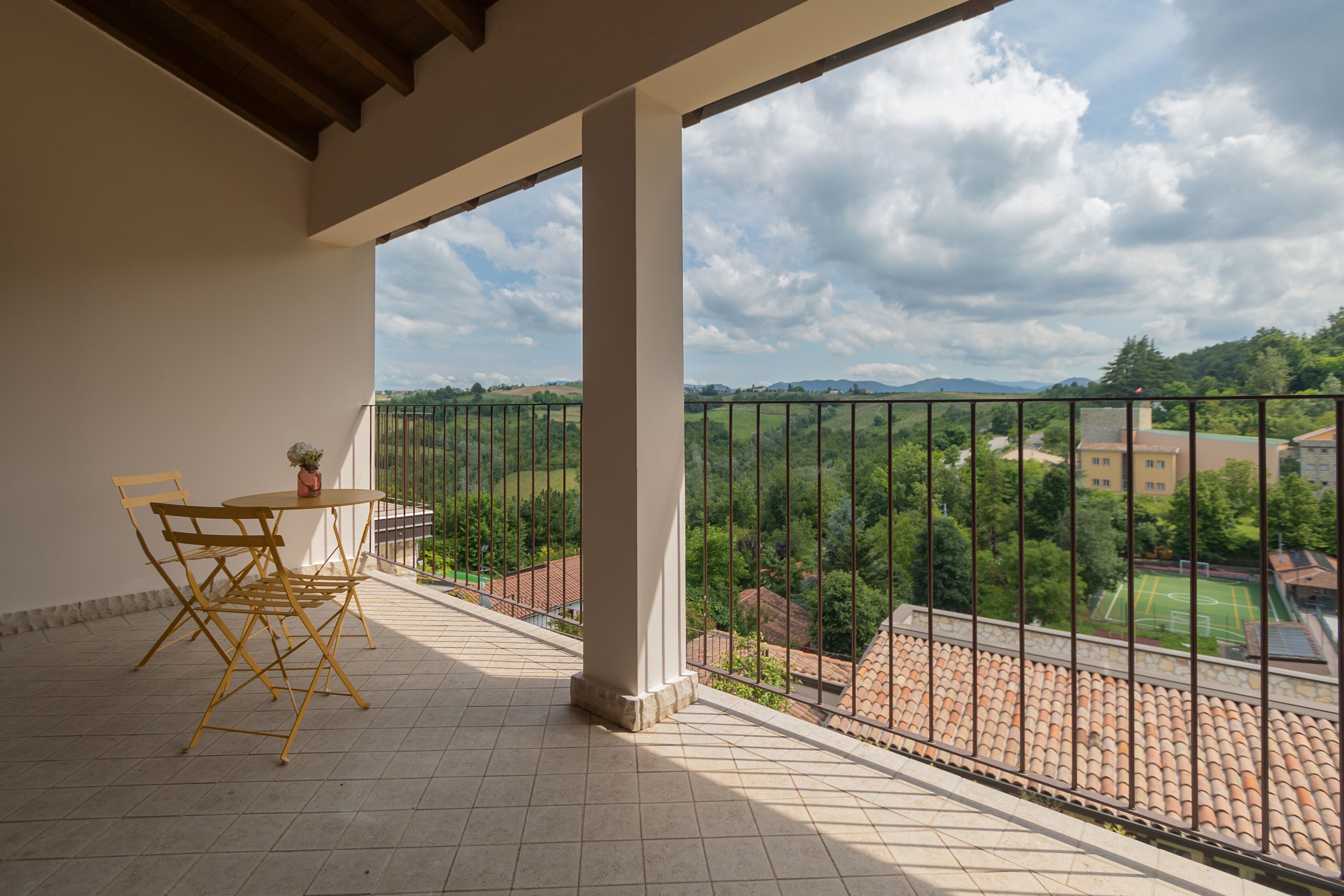 A balcony with a table and chairs, a view of a green landscape, and a cloudy sky.