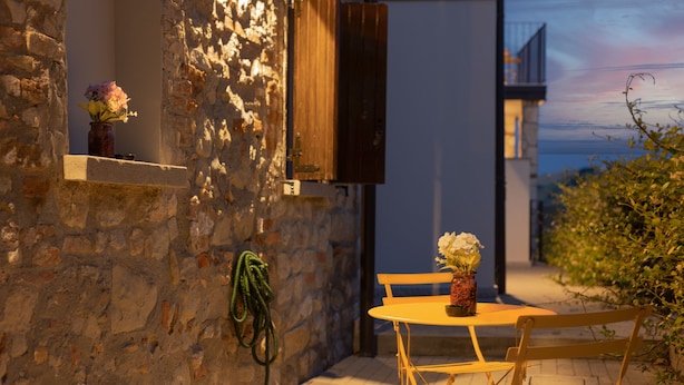 A stone wall with a wooden door, a small table with chairs, and a vase with flowers. - Luce Boutique Hotel (Fortunago)