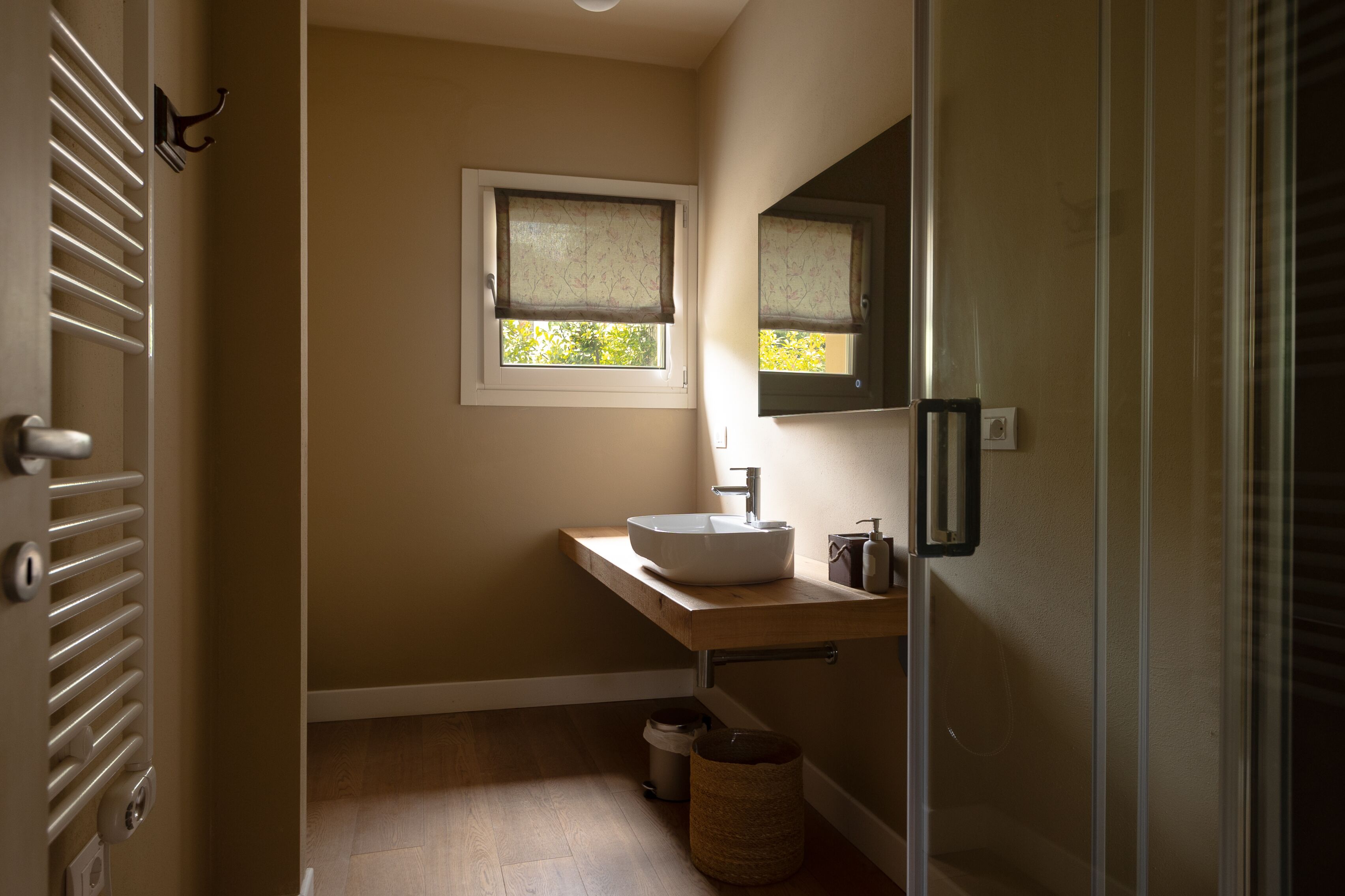 A bathroom with a wooden vanity, a white sink, a mirror, and a window with blinds.