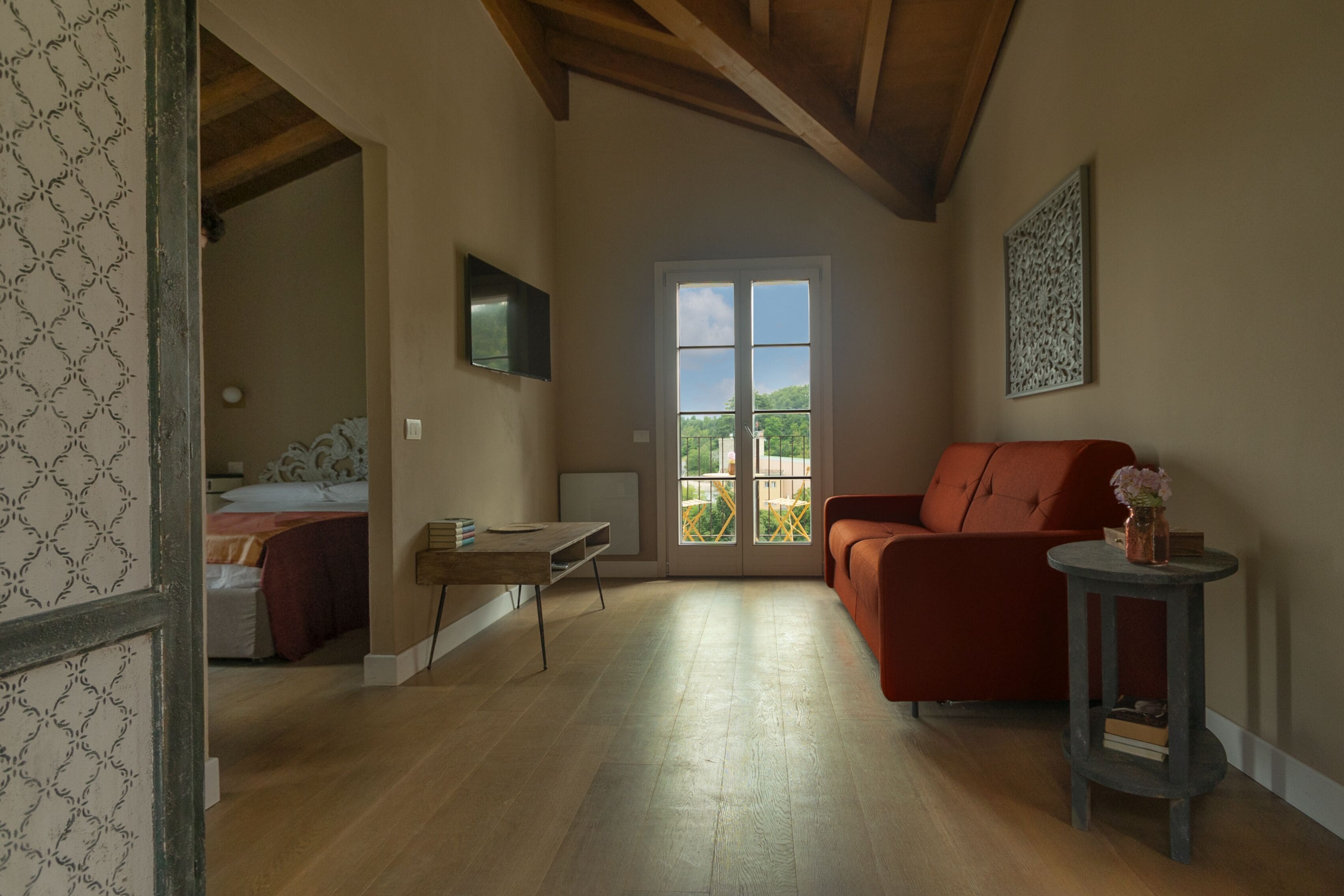 Ein geräumiger Raum mit Holzboden, einem roten Sofa, einem kleinen Tisch mit einer Vase und einem Bett mit einem gemusterten Kopfteil.