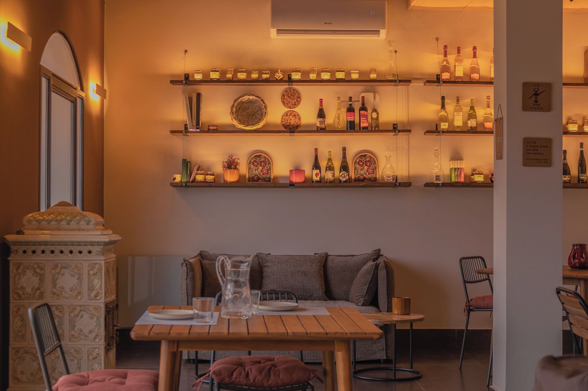 A cozy dining area with a wooden table, cushioned seating, and shelves with bottles and decorative items.