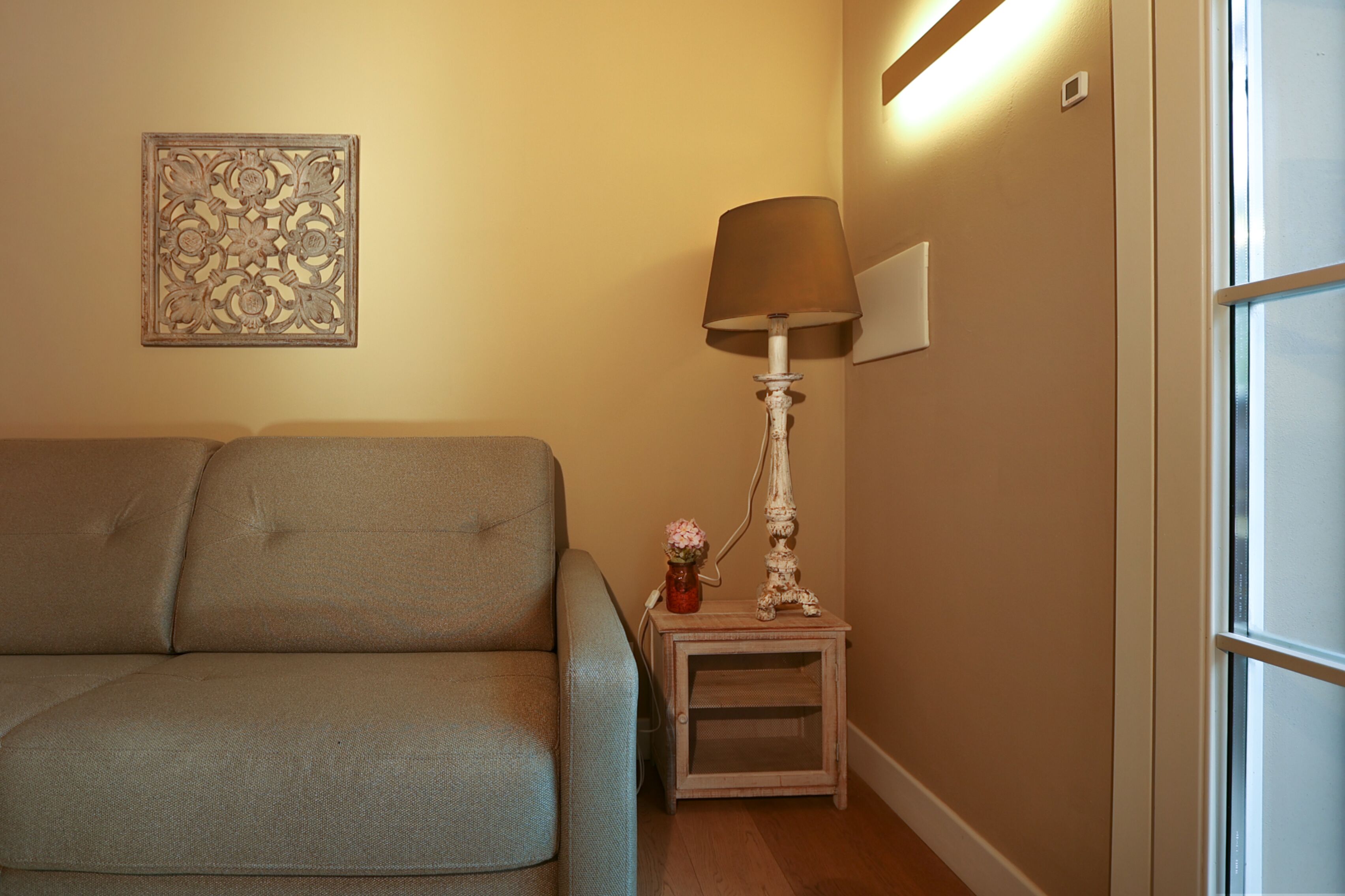 A living room with a sofa, a small table with a lamp, and a decorative wall piece.