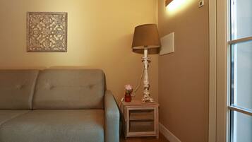 A living room with a sofa, a small table with a lamp, and a decorative wall piece.