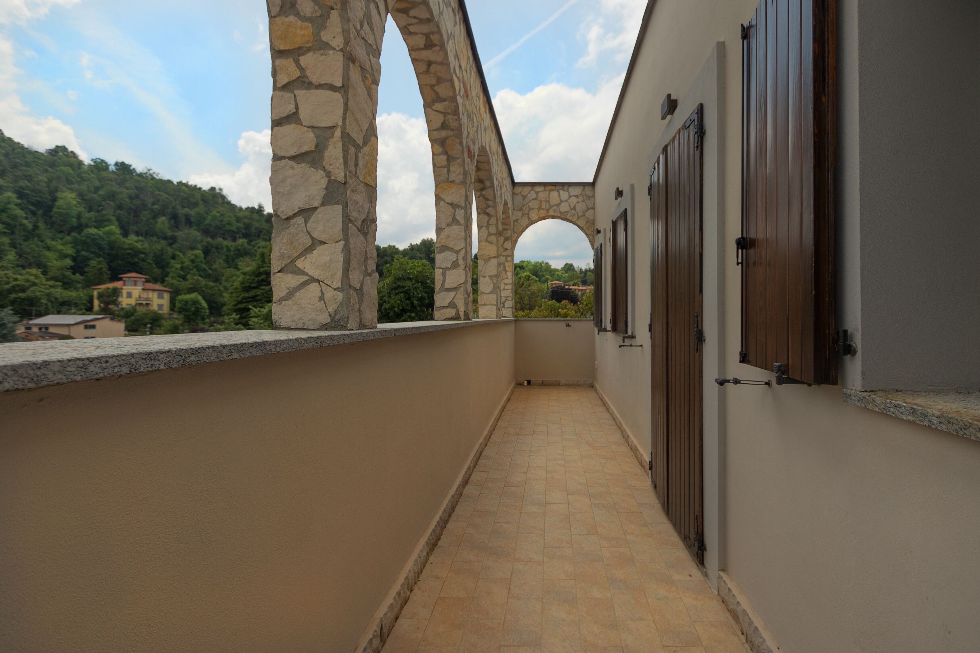 Un couloir orné d’arches en pierre, doté d’un sol carrelé et offrant une vue sur une colline verdoyante.
