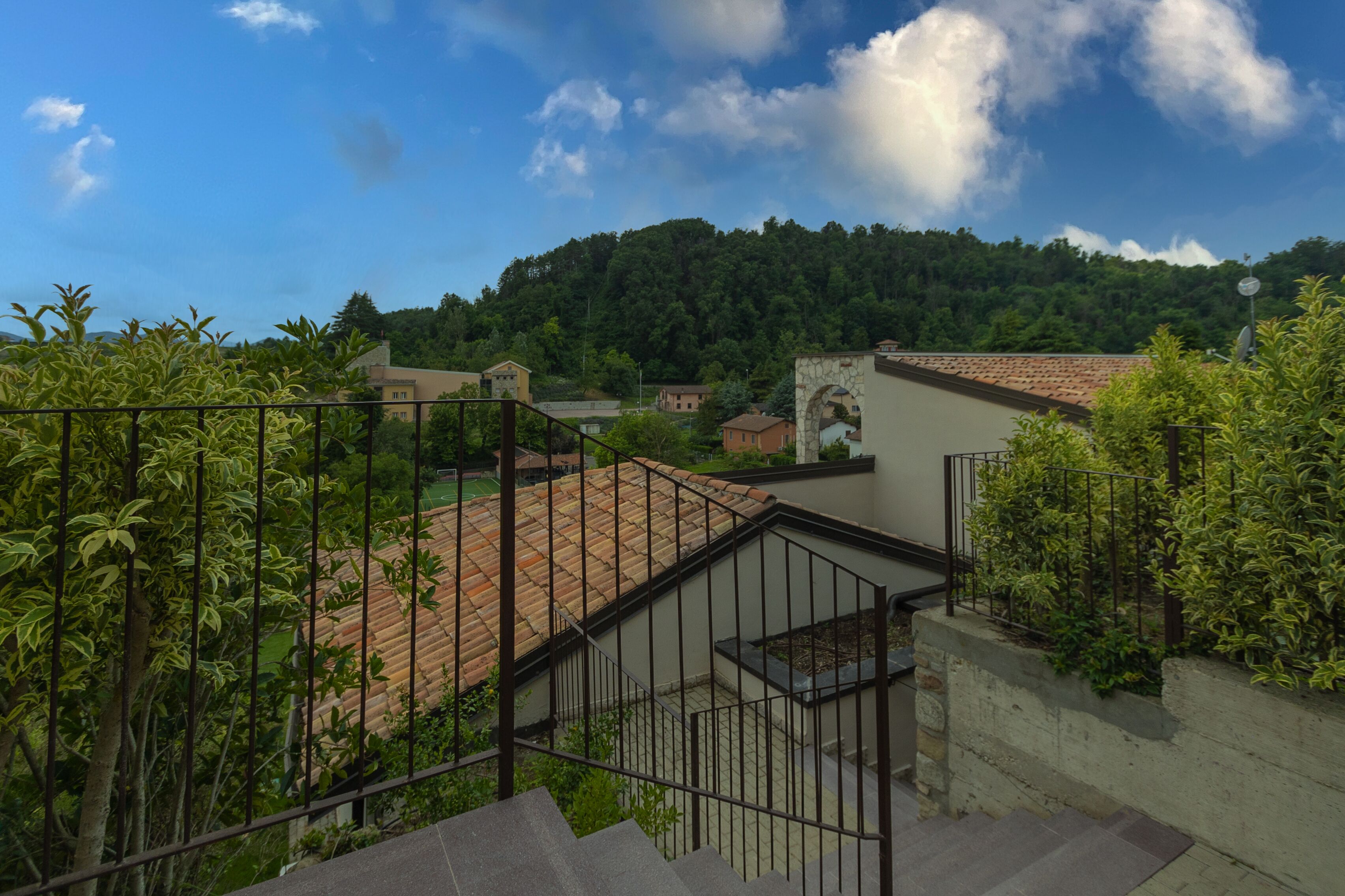 Zona residencial con una escalera que lleva a una terraza, rodeada de vegetación y una colina al fondo.