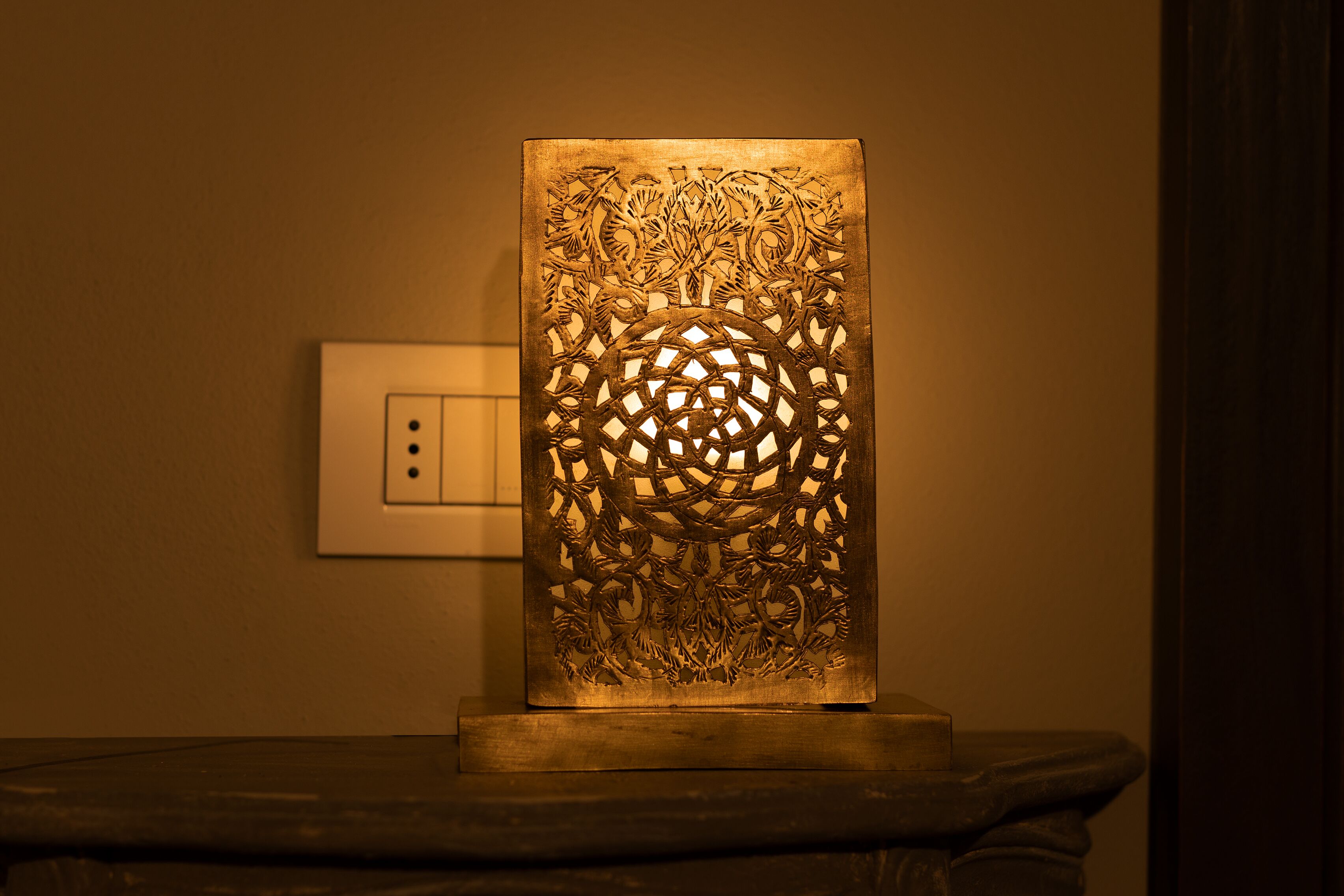 Un adorno de pared con diseños tallados complejos y una fuente de luz detrás, montado sobre una superficie oscura.