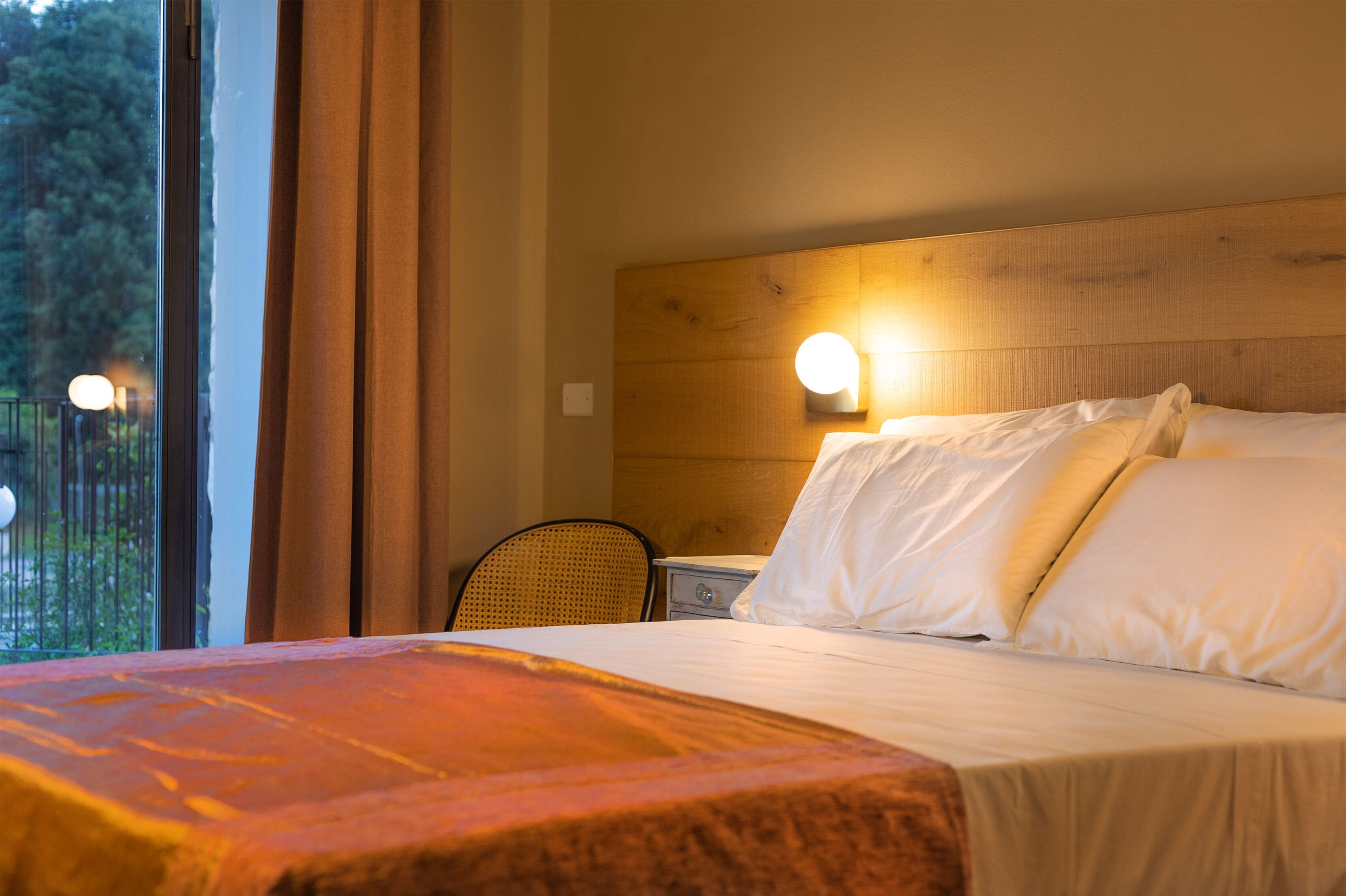 Ein Hotelzimmer mit hölzernem Kopfteil, einem Bett mit weißer Bettwäsche, einem Nachttisch und einem Sessel.