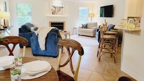 A spacious living room with a fireplace, a dining area with a table set for four, and a kitchen area with bar stools. - Family-sized beach house with pool; walk to beach and restaurants (St. Augustine)