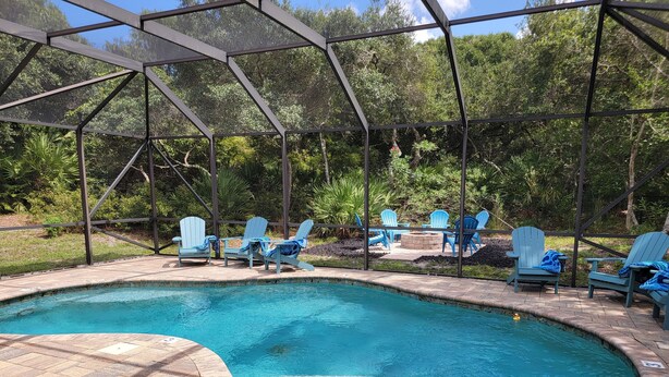 A swimming pool with blue Adirondack chairs and a fire pit area, surrounded by a metal fence and lush greenery. - Family-sized beach house with pool; walk to beach and restaurants (St. Augustine)
