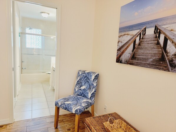A room with a wooden floor, a patterned chair, a glass shower enclosure, and a beach scene painting on the wall. - Family-sized beach house with pool; walk to beach and restaurants (St. Augustine)
