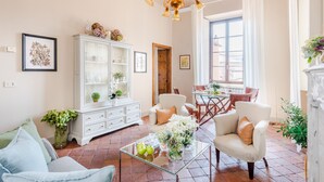 A spacious living room with a glass coffee table, white armchairs, a white cabinet, and a dining area with a table and chairs. - Antico Sogno Penthouse (Lucca)