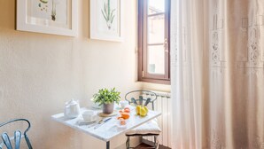A dining area with a table set for two, a potted plant, and a window with curtains. - Antico Sogno Penthouse (Lucca)