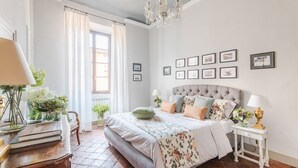 A bedroom with a large bed, a chandelier, and framed pictures on the wall. - Antico Sogno Penthouse (Lucca)
