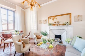 A living room with a fireplace, comfortable seating, and a dining area with a table set for four. - Antico Sogno Penthouse (Lucca)