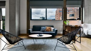 A modern living room with a sofa, two chairs, a coffee table, and a large window with a city view.