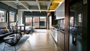 A modern kitchen with a refrigerator, wooden cabinets, and a dining area with a sofa and chairs.