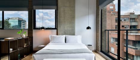 A modern bedroom with a large bed, a wooden bench, a bedside table, a potted plant, and a view of the city through large windows.