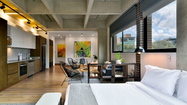 A modern hotel room with a large bed, a desk, a chair, and a view of the city.