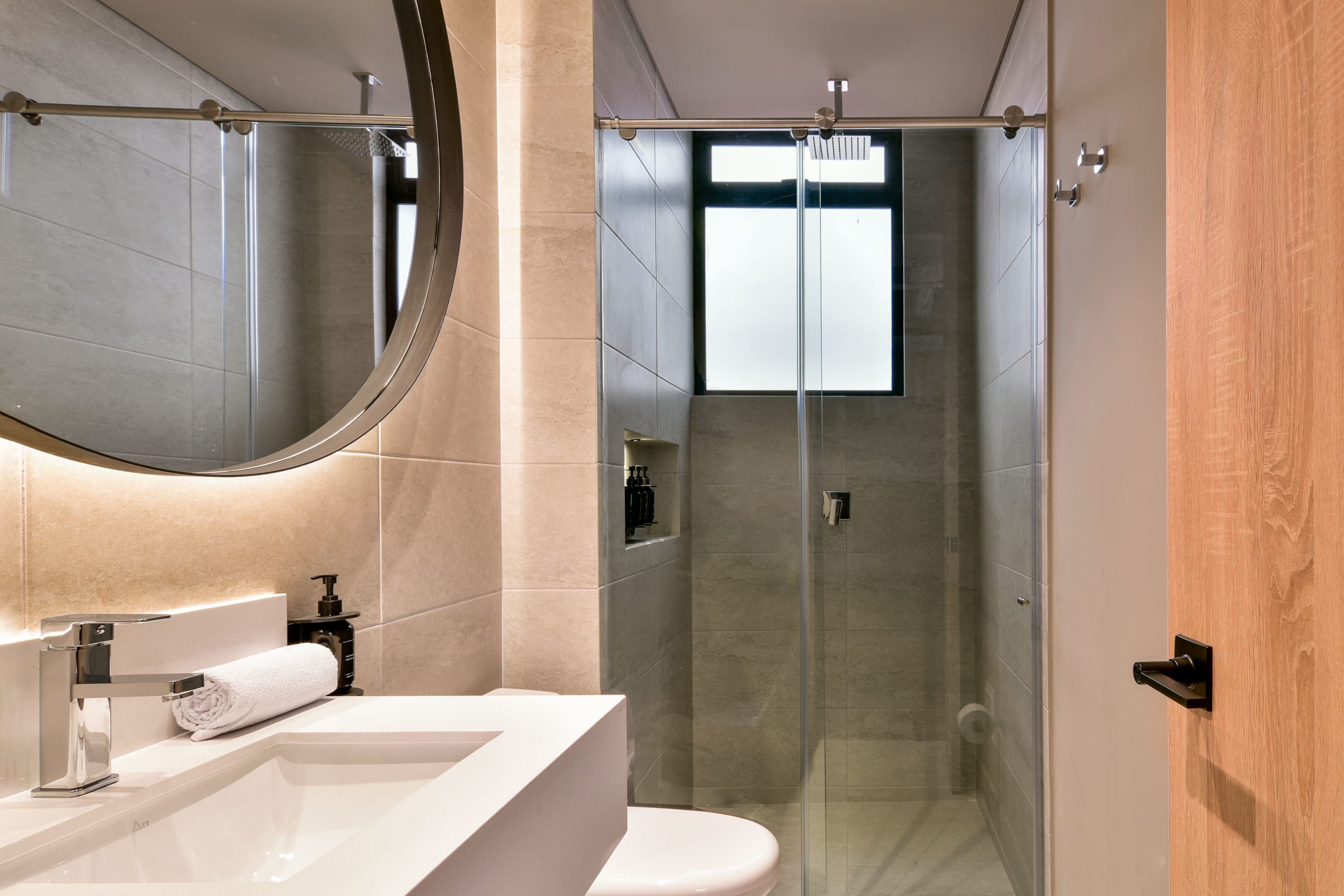 A modern bathroom with a white sink, a large mirror, and a glass-enclosed shower.