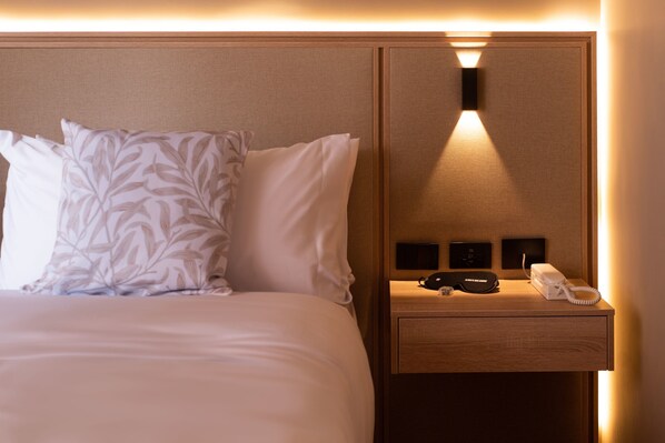 Une chambre d’hôtel avec un lit bien fait, une table de chevet avec un téléphone et une petite enceinte, et un luminaire fixé au mur.