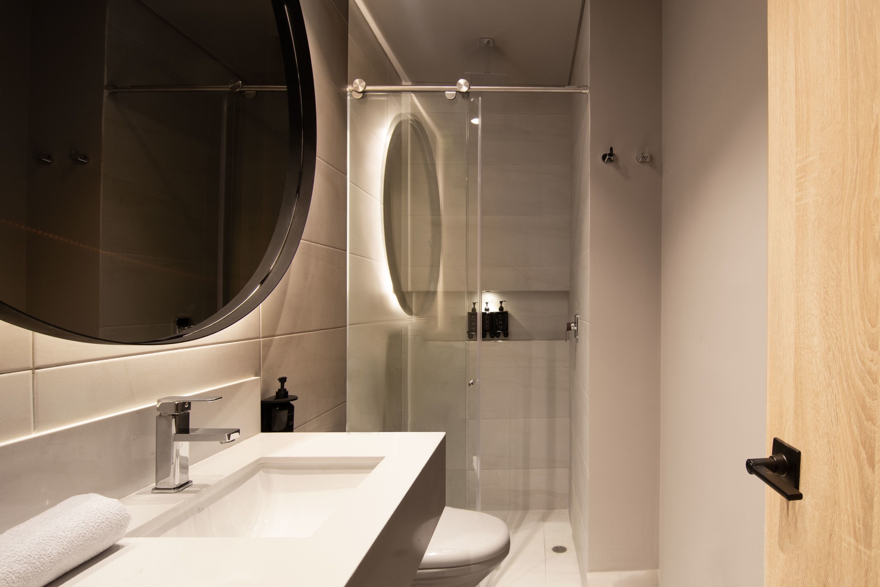 A modern bathroom with a large mirror, a white sink, and a glass-enclosed shower.