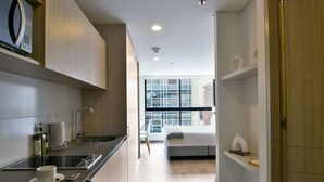 A modern kitchen with a built-in microwave, a sink, and a countertop with a cup and a bottle. There is a bed with a white blanket and a window with a view of buildings. - w Magnificent Loft w City View in Santa Barbara (Bogotá)