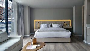 Habitació d'hotel moderna amb un llit gran, un escriptori i vista a la ciutat per la finestra.