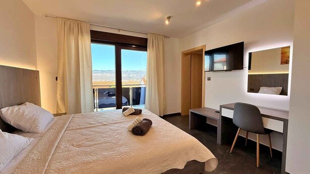 Et hotelværelse med seng, skrivebord, stol og udsigt over byen.