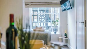 A hotel room with a bed, a window with a view of a building, a flat-screen TV mounted on the wall, and a bottle of champagne on a small table. - NEW! Stunning Studio in the City-Centre, Sleeps 2! (Chester)