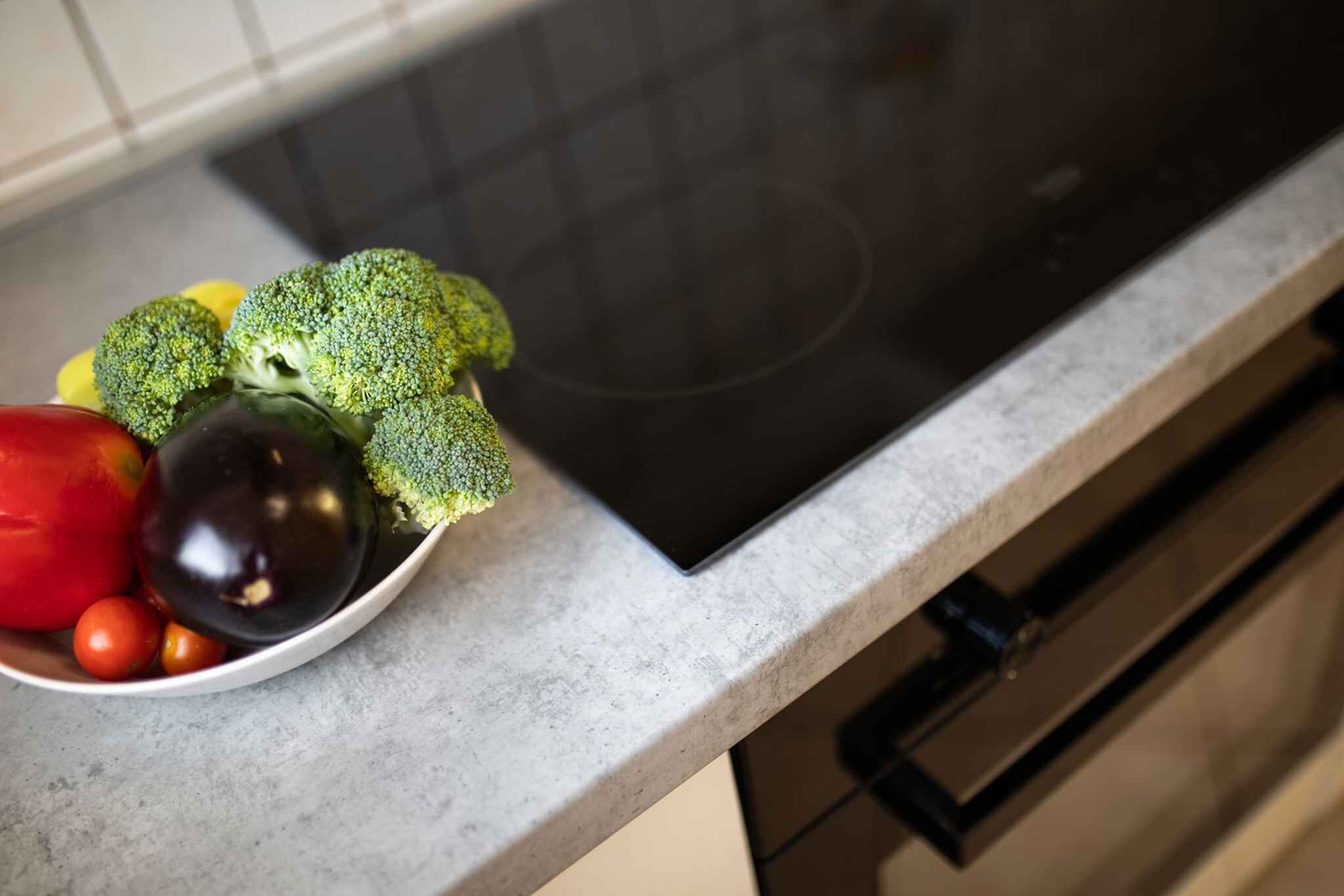 Una encimera de cocina con un tazón de verduras y una placa de inducción negra.
