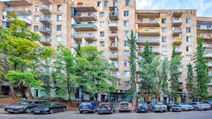 A multi-story residential building with balconies, a parking area, and trees along the street. - HB apartments Mtskheta (Tbilisi)