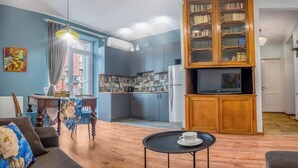 A living room with a sofa, a small table with a cup, a wooden cabinet with books, and a kitchen in the background. - HB apartments Mtskheta (Tbilisi)