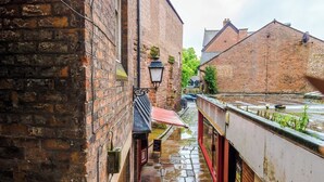 A narrow alleyway with brick buildings, a red awning, and a metal railing.